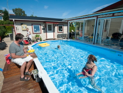 En familj vid sin pool, en friggebod syns i bakgrunden