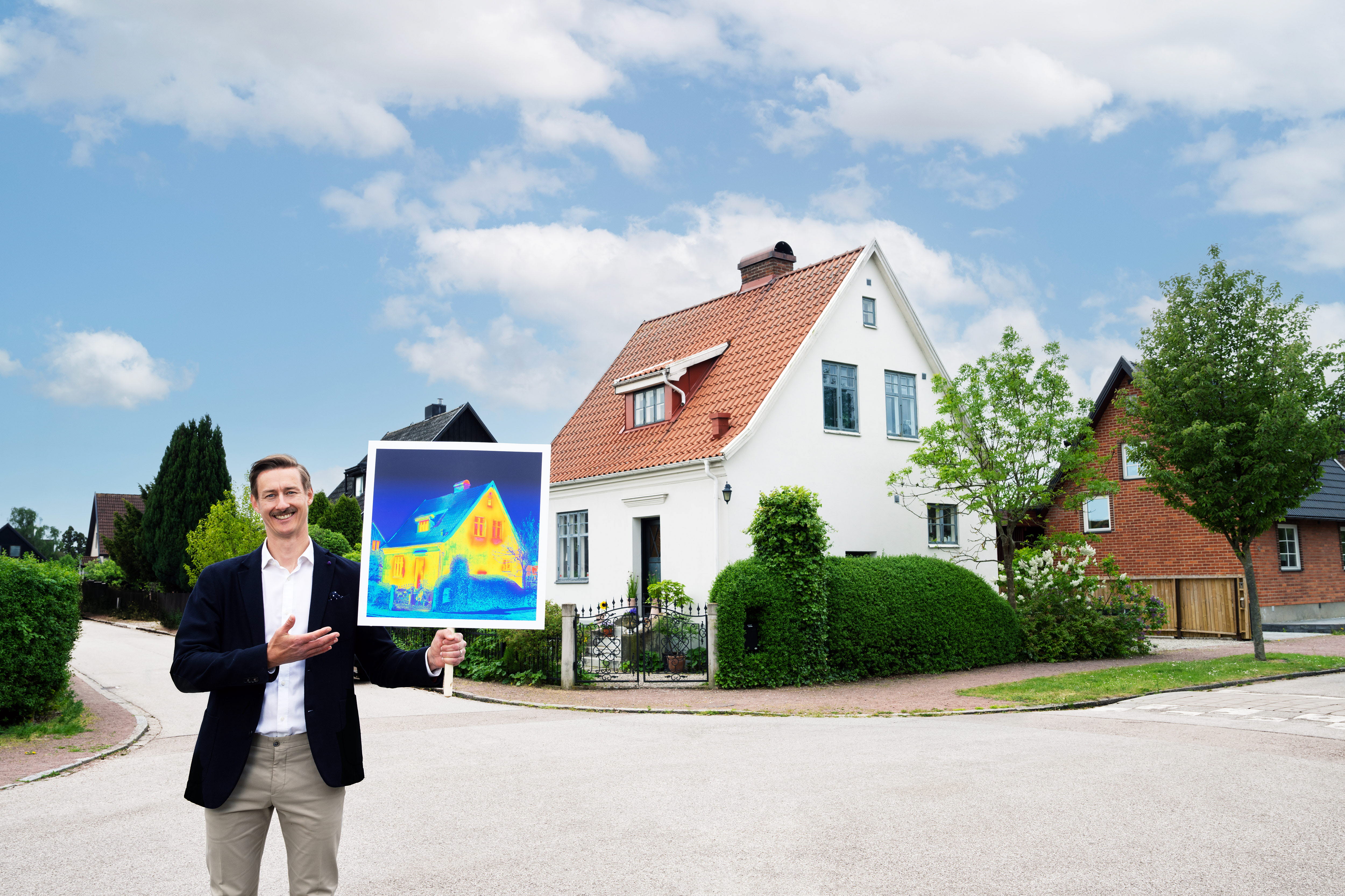 Man som står framför ett hus och håller en skylt i handen.