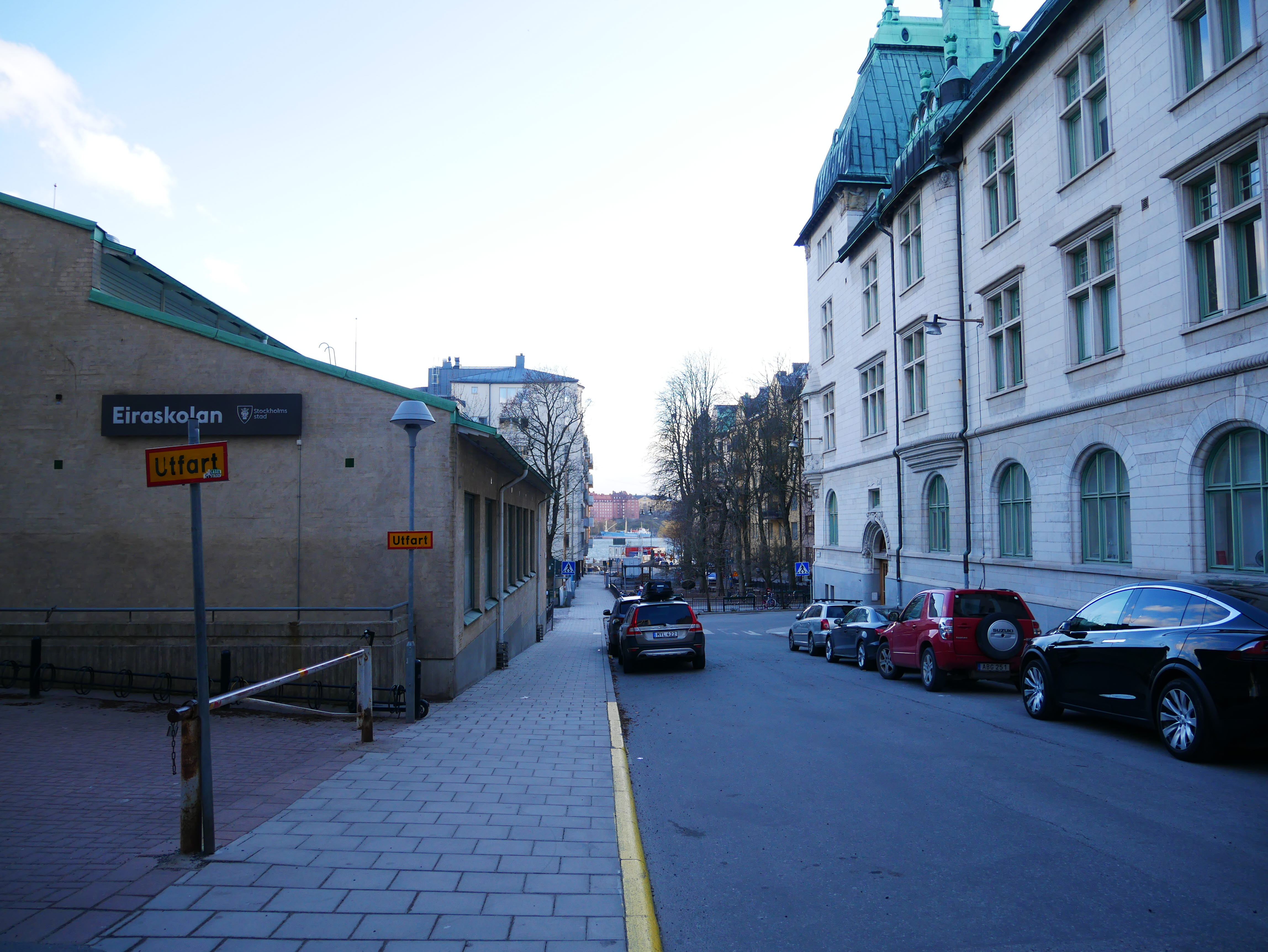 Foto på en gata med byggnader, asfalt, bilar och trottoar.