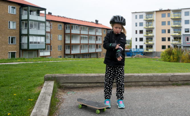 Barn med skateboard på en gård framför flerbostadshus. Foto: Franz Feldmanis.