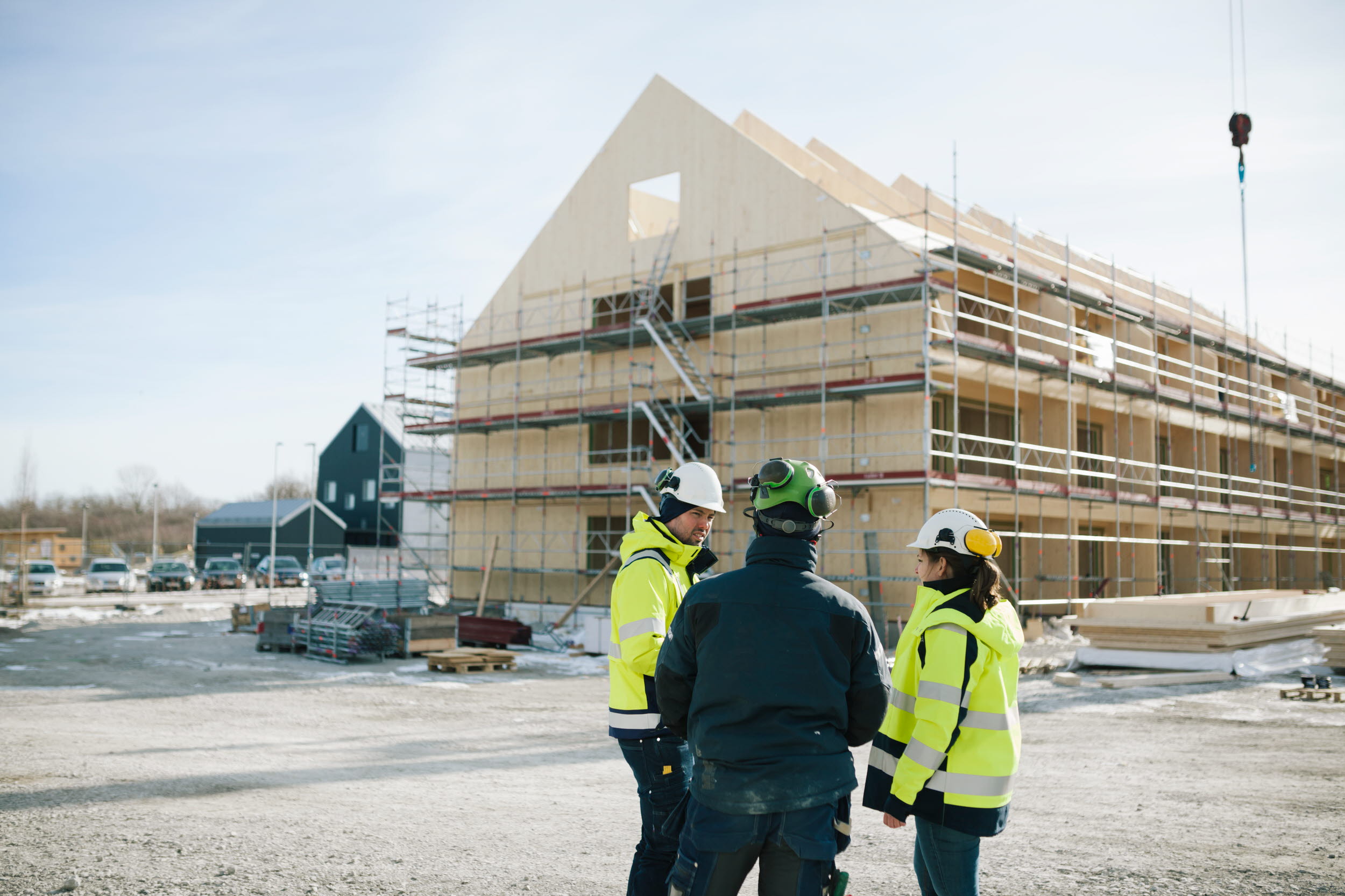 Byggarbetare i varselkläder framför träbyggnad under uppförande.