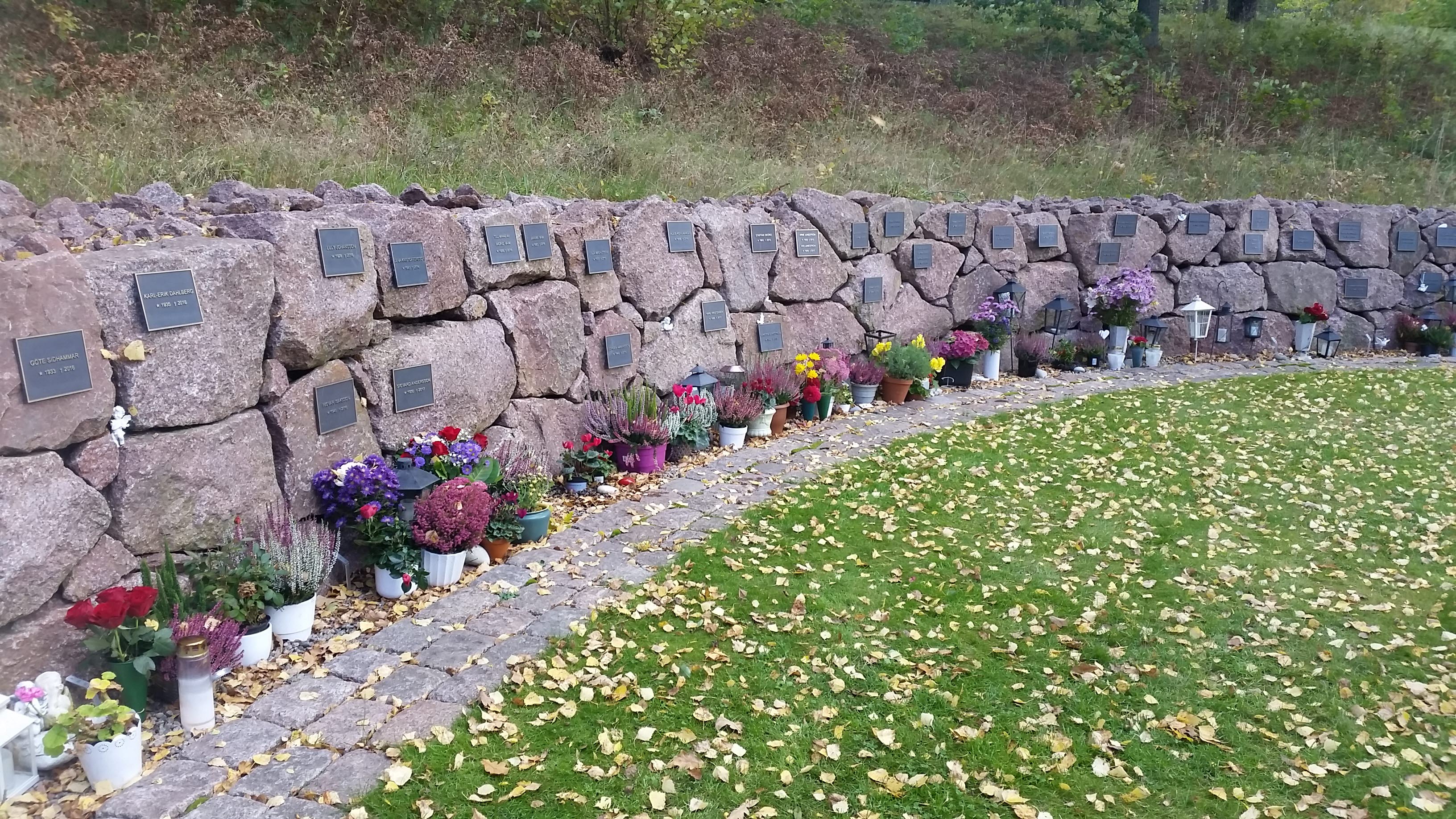 Foto på urngravplats i form av en stenmur med plaketter och blomvaser.