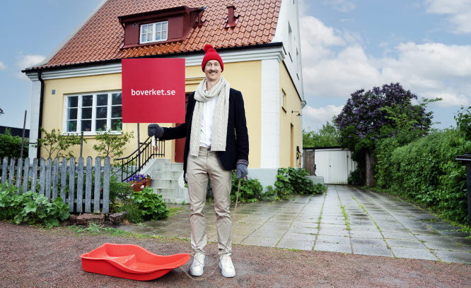 Man med skylt framför hus. På skylten står det boverket.se/energiuiden.