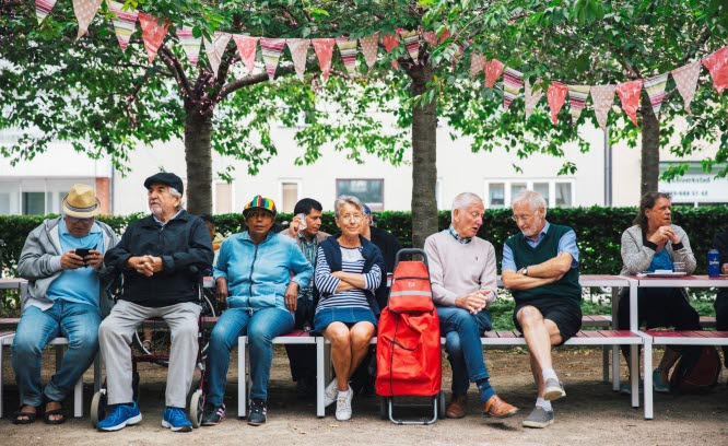 Människor på parkbänkar med flaggspel i träden