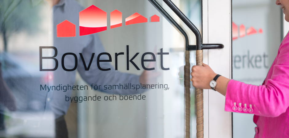 Kvinna öppnar glasdörr med Boverkets logotype