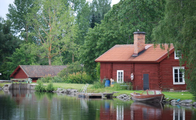 Foto på äldre byggnad i grönområde intill vatten