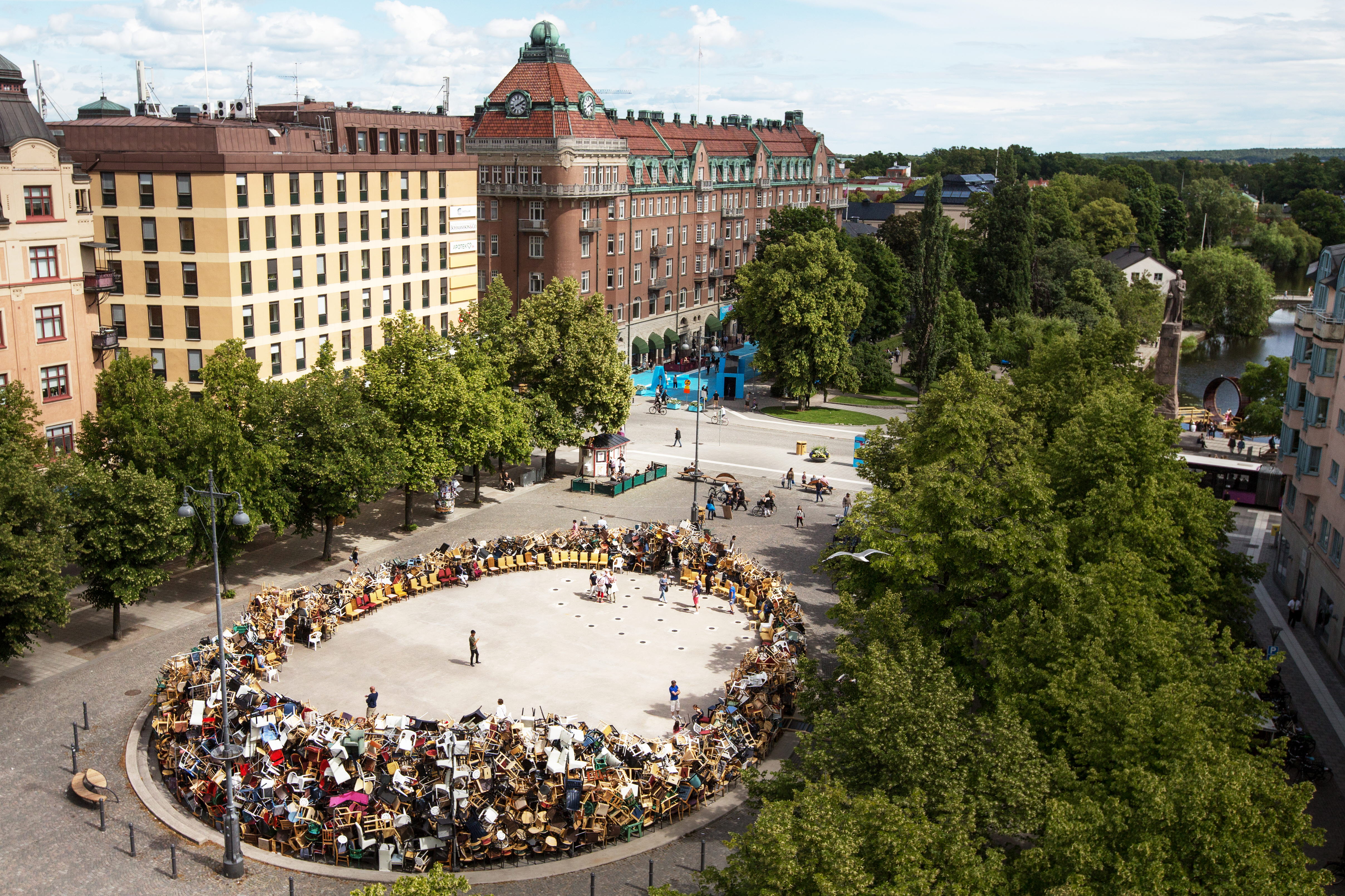 Foto på konstverk med tusentals stolar på ett stor torg.