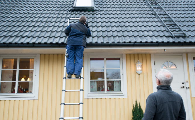 Man står på en stege och inspekterar takpannor.