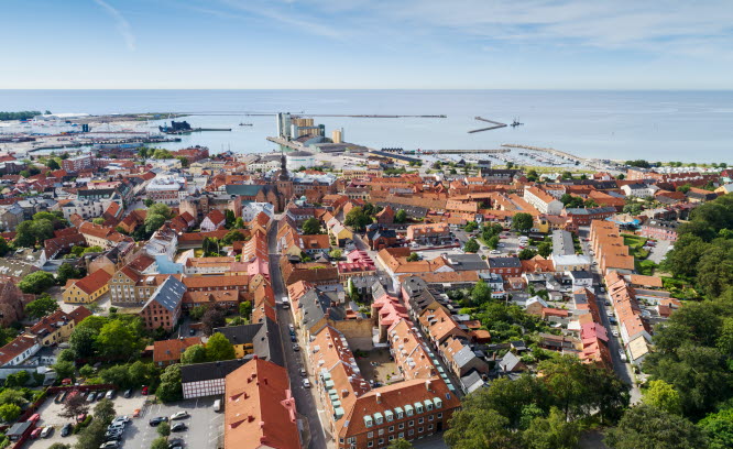 Flygfoto över stad med bostäder, lokaler industri och hamn med mera