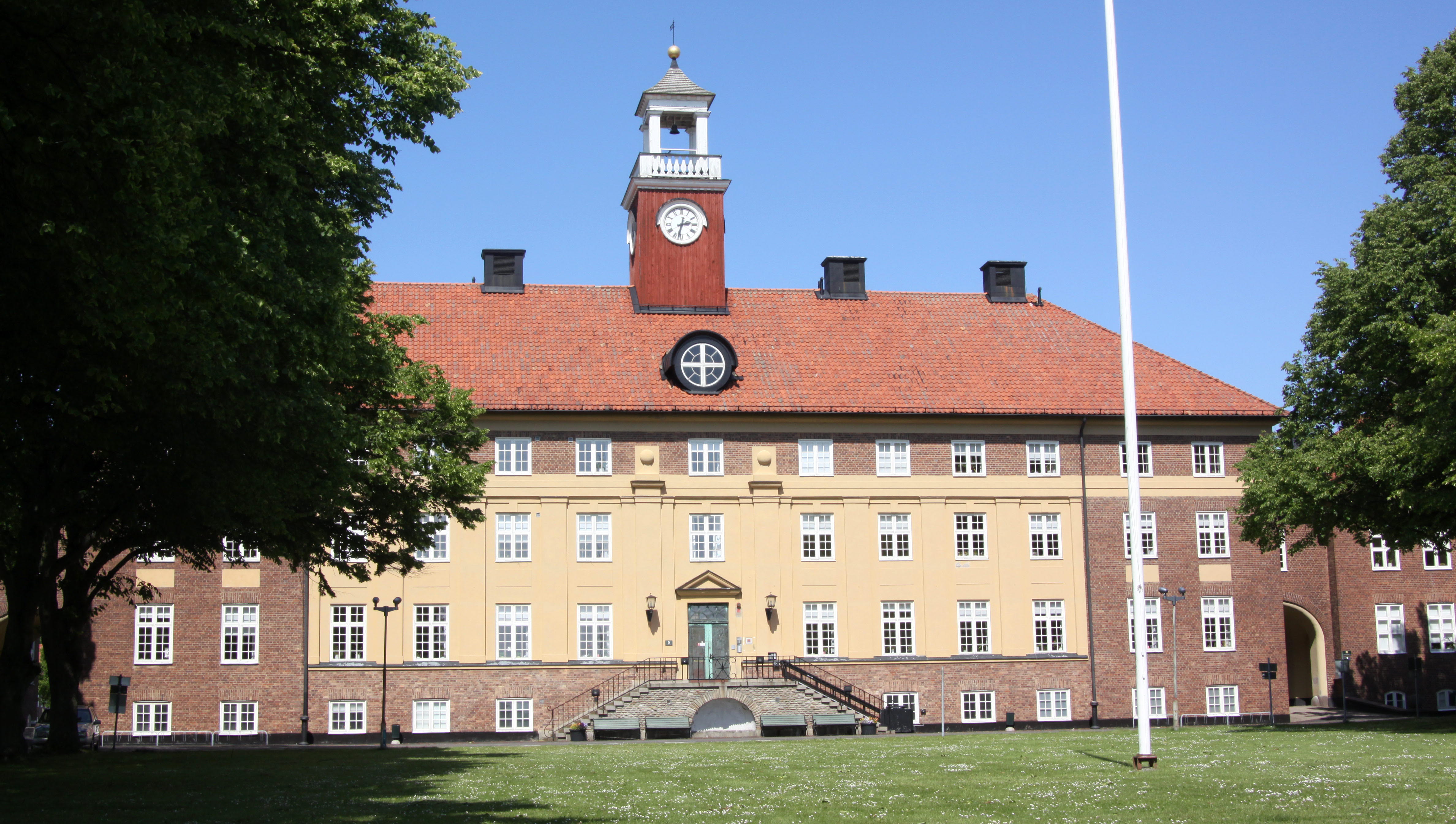 Stor tegelbyggnad i 4 våningar med klocktorn på taket.