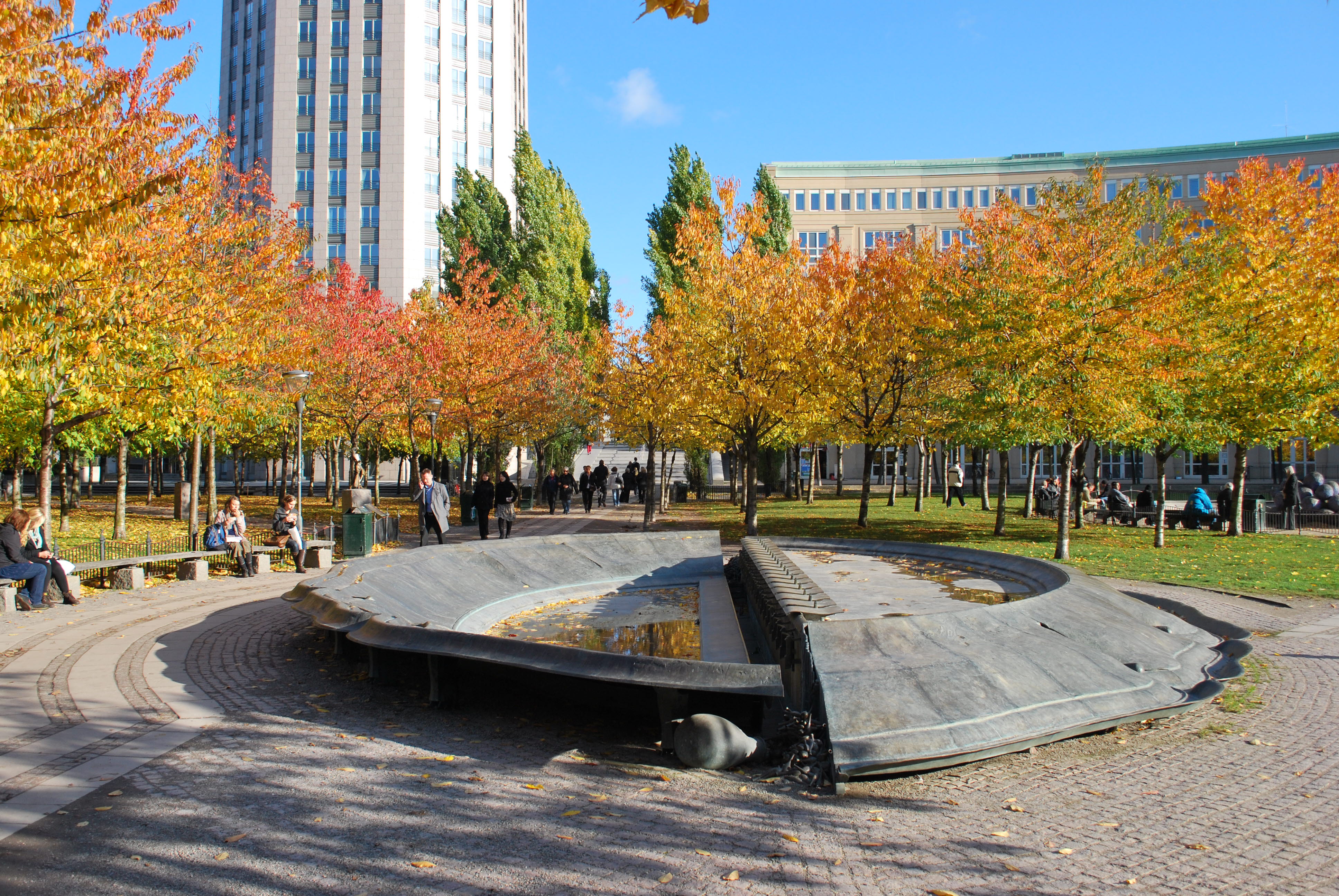 Runt monument på en rund stensatt yta. Trädrader runt om.