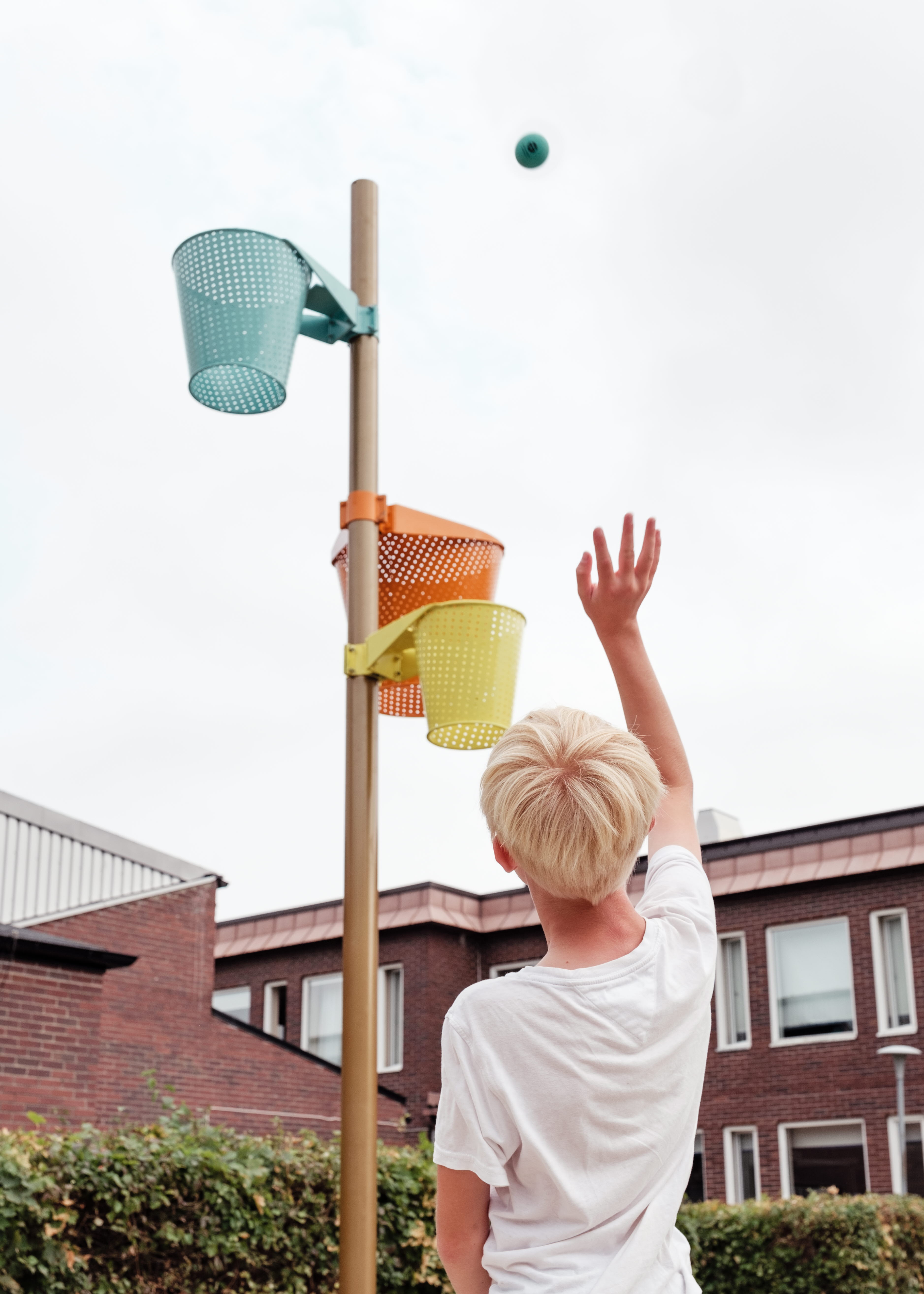 Pojke som kastar en liten blå boll mot tre basketkorgar i olika färger. Den blå bollen är på väg mot den blå basketkorgen.