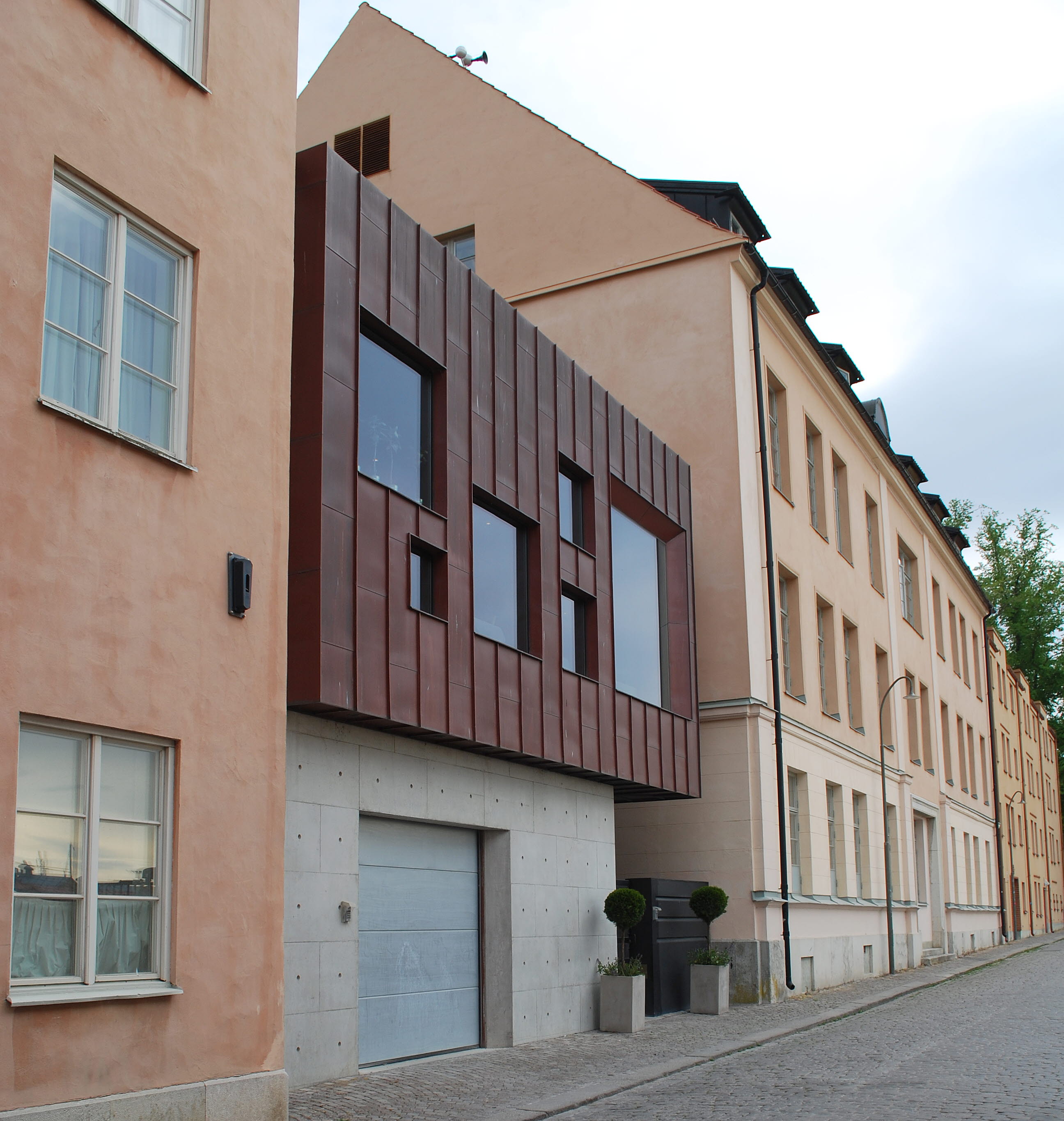 En gatstensbelagd gata med fastigheter på båda sidor. På vänstesidan syns en tillbyggnad i kopparplåt och betong.