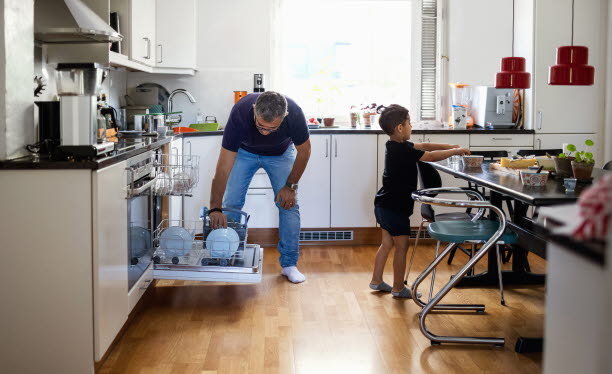 Pappa plockar ur diskmaskinen och sonen dukar i köket.