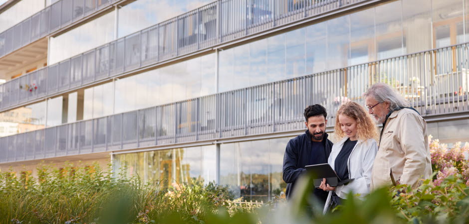 Tre personer tittar på en läsplatta utanför ett flerbostadshus.