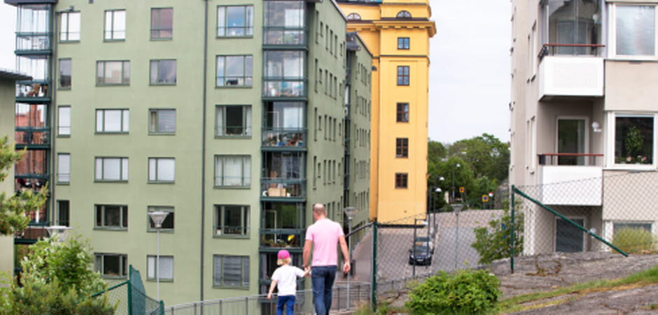 Man och barn hand i hand framför flerbostadshus. 