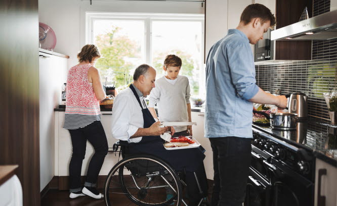 En man i rullstol jobbar i köket tillsammans med sin familj.