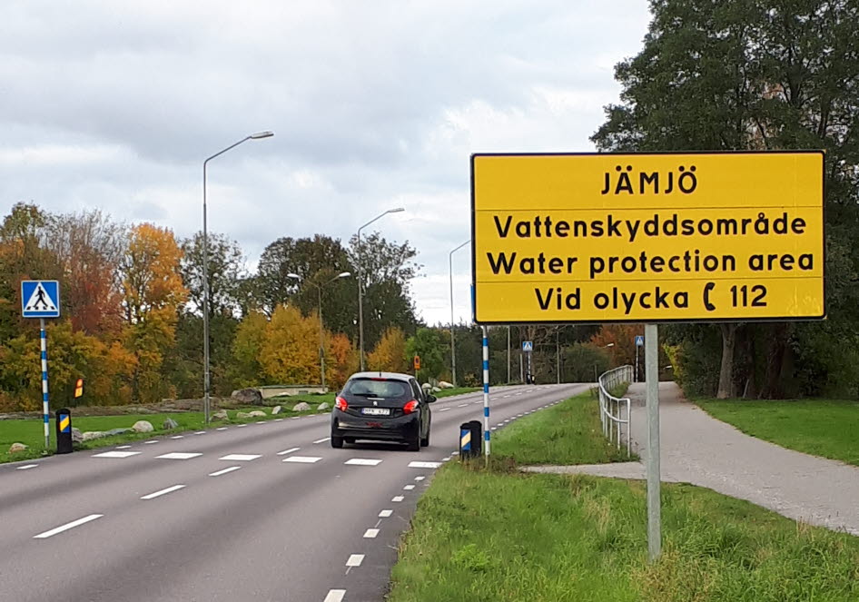 Varningsskylt för vattenskyddsområde. Skylten står vid en väg med övergångsställe.