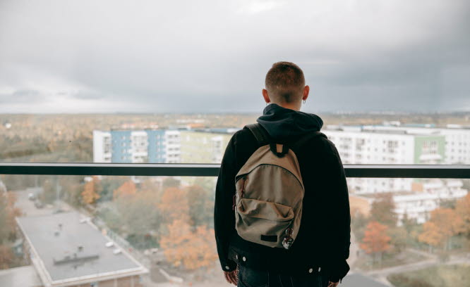 Ett barn står på en balkong och ser ut över ett bostadsområde. Foto: Scandinav