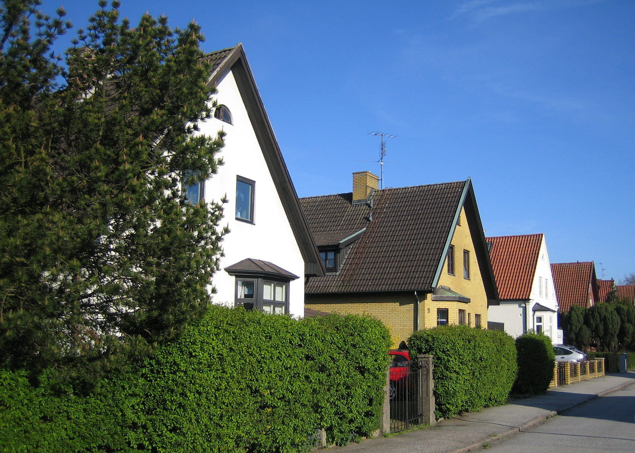 Villagata med hus längsmed, häckar och buskar.