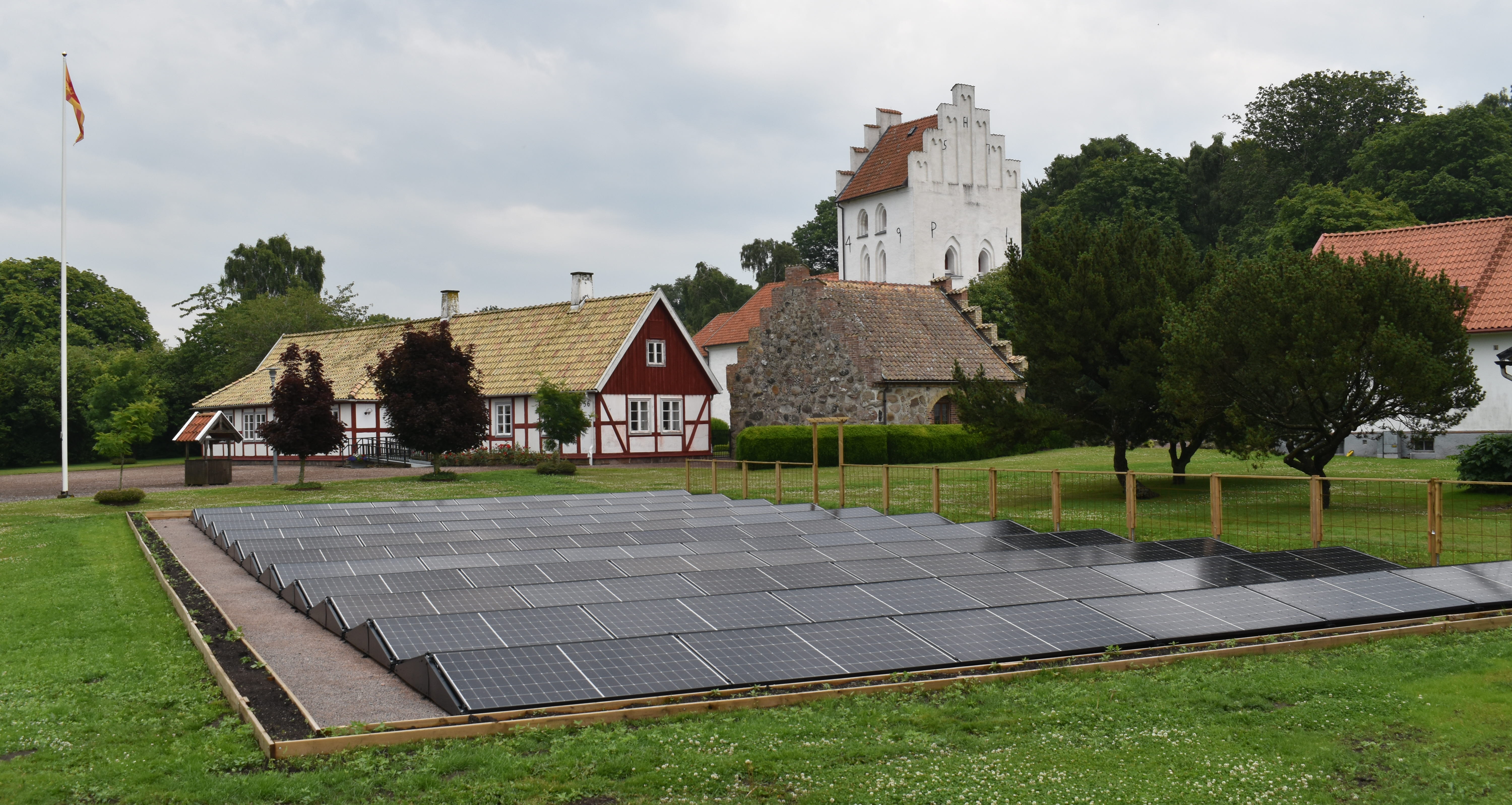 Solpaneler på en gräsmatta framför ett bostadshus och en kyrka. 