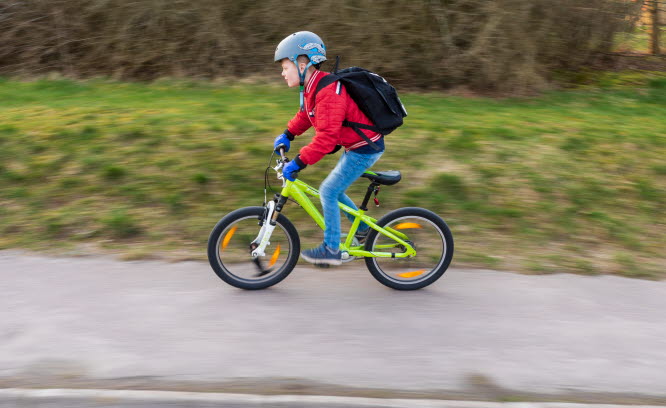 Pojke på grön cykel som cyklar på en trottoar.