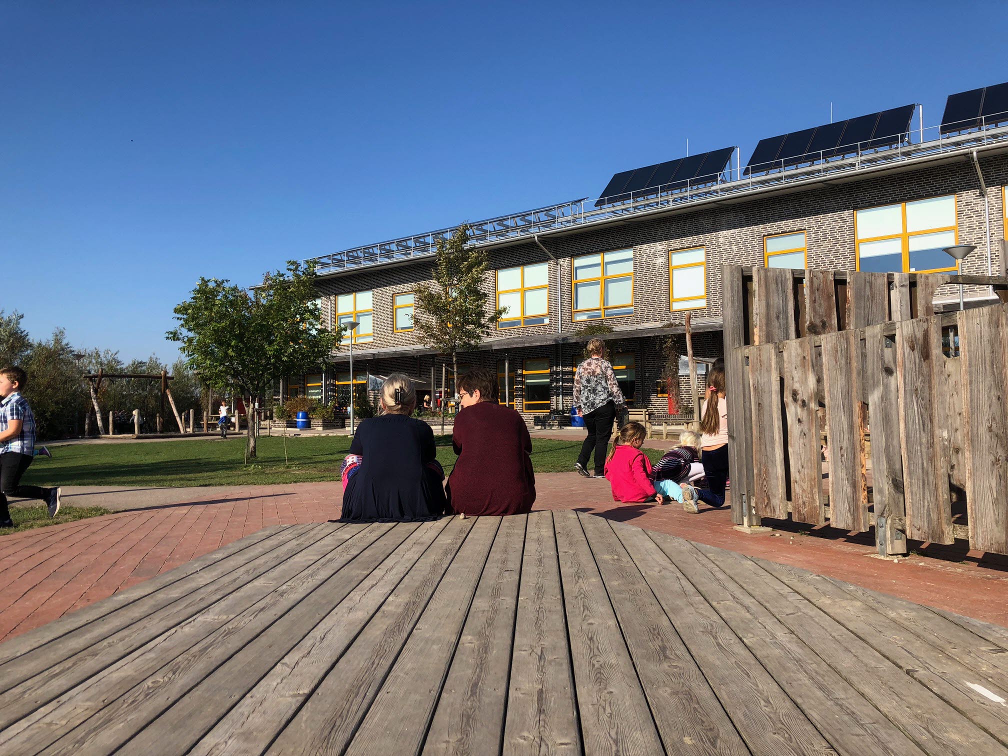 Vuxna människor som sitter på ett trädäck och blickar ut över skolgården.