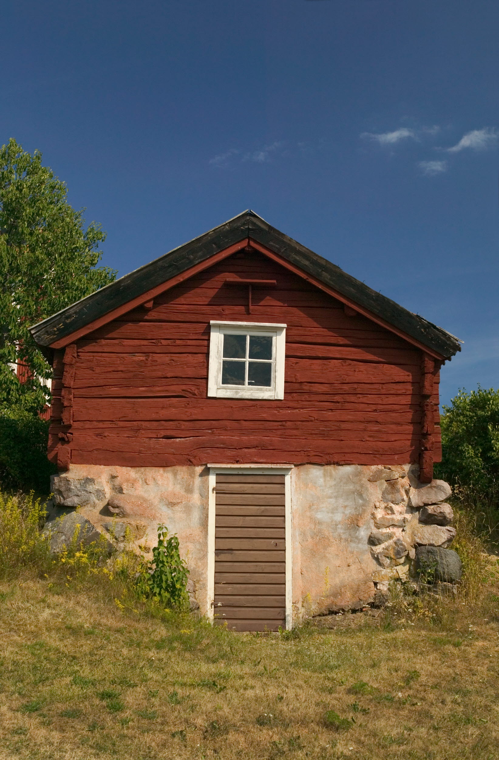 Röd stuga med en äldre källarvägg av sten