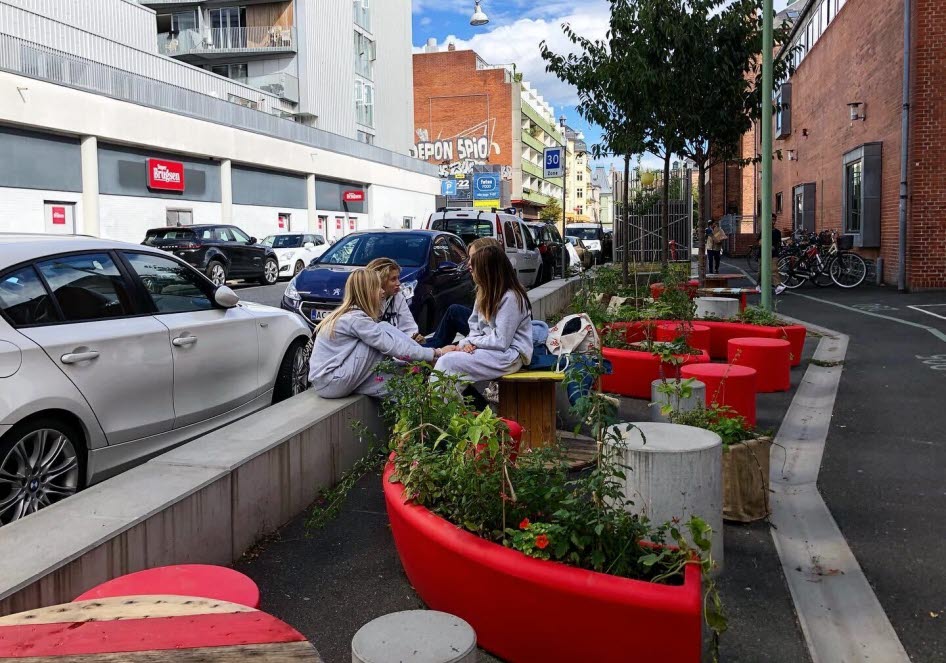 Ungdomar som sitter i en pocket-park intill en väg i stadsmiljö.