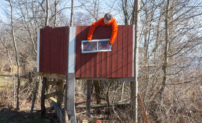 Ett barn i orange jacka som håller upp ett fönster på en trädkoja.