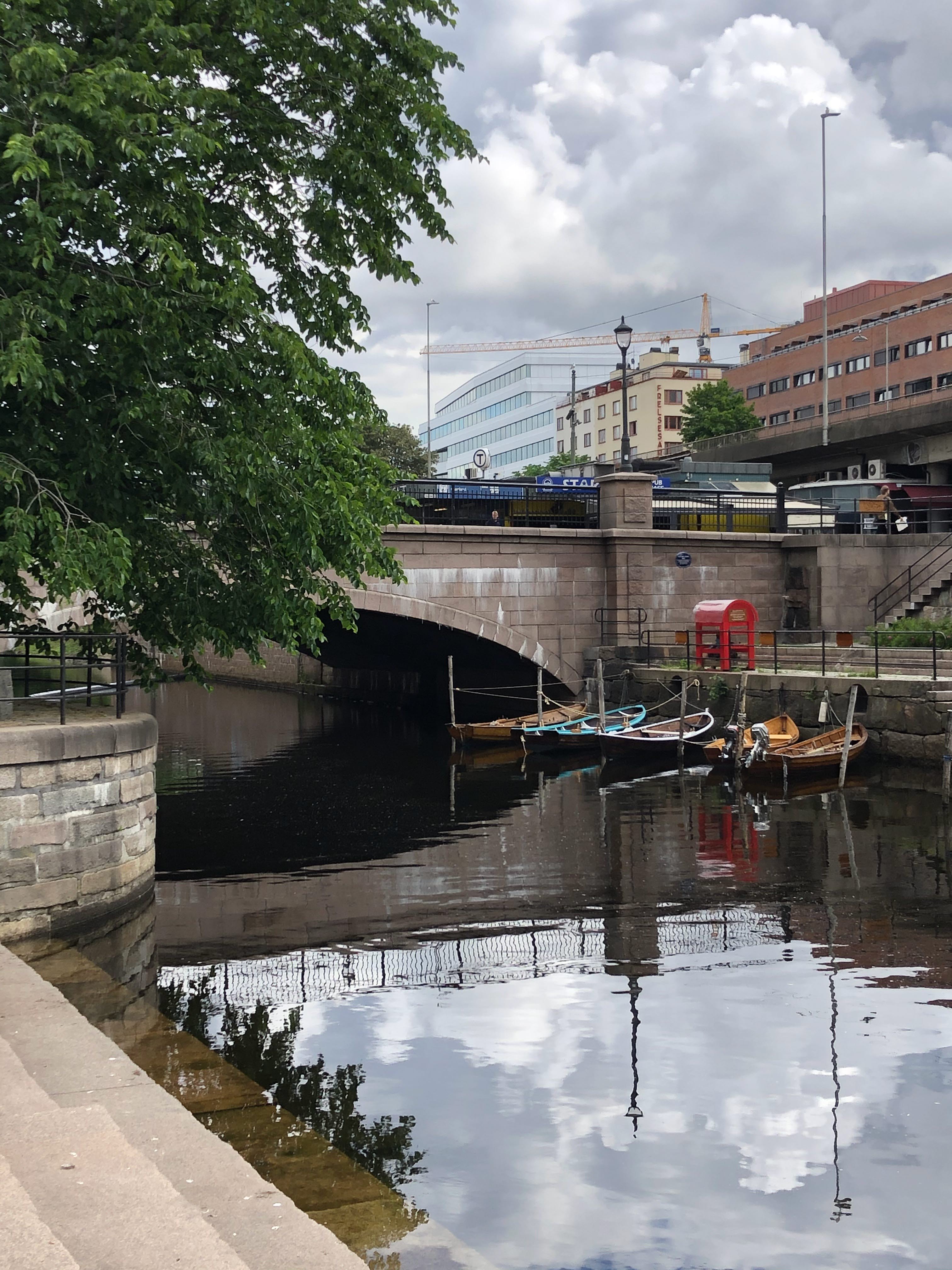 Båtar i älv framför en stenbro. I förgrunden en stentrappa ner mot vattnet.