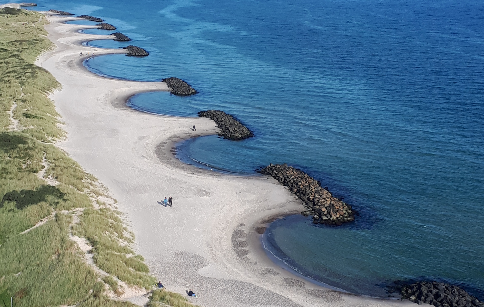 En rad av vågbrytare bestående av stenblock har anlagts utmed sandstranden. Sand har eroderats i mellanliggande områden.