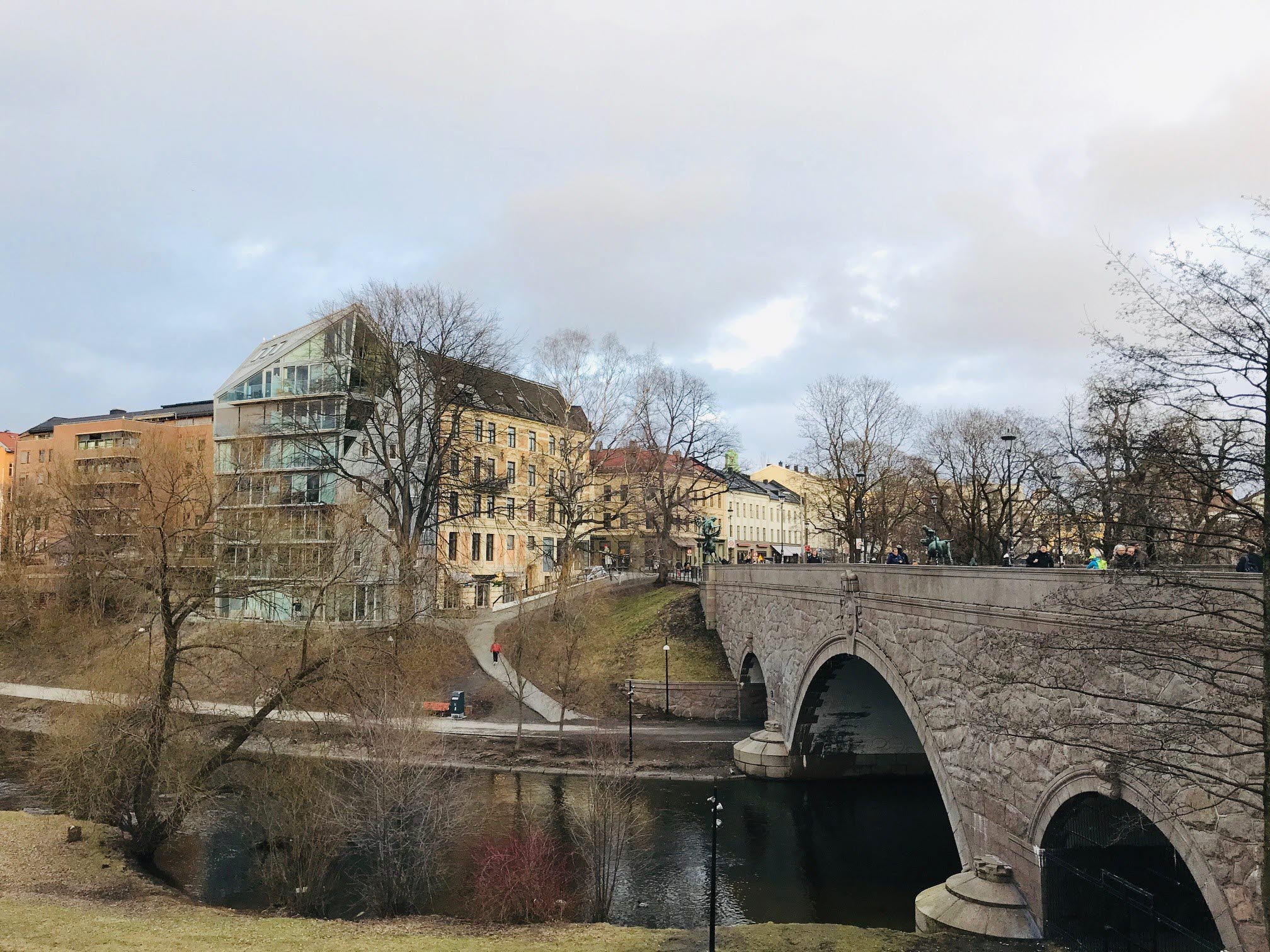 Stenbro över älv mot bostadsområde med flerfamiljshus.