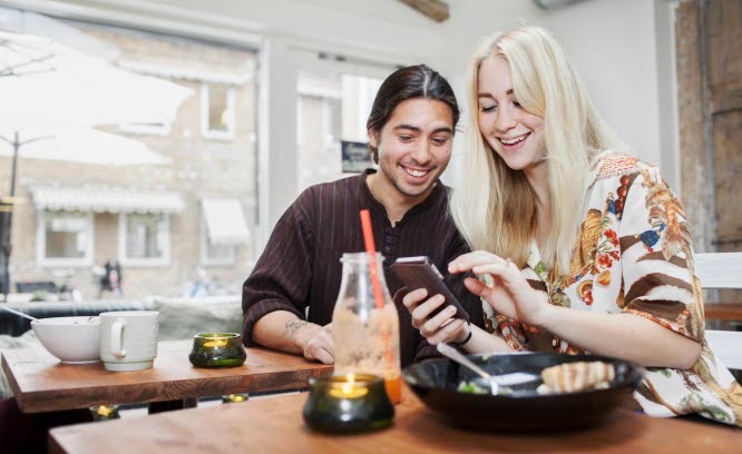 Två ungdomar umgås på café och tittar på en smartphone.