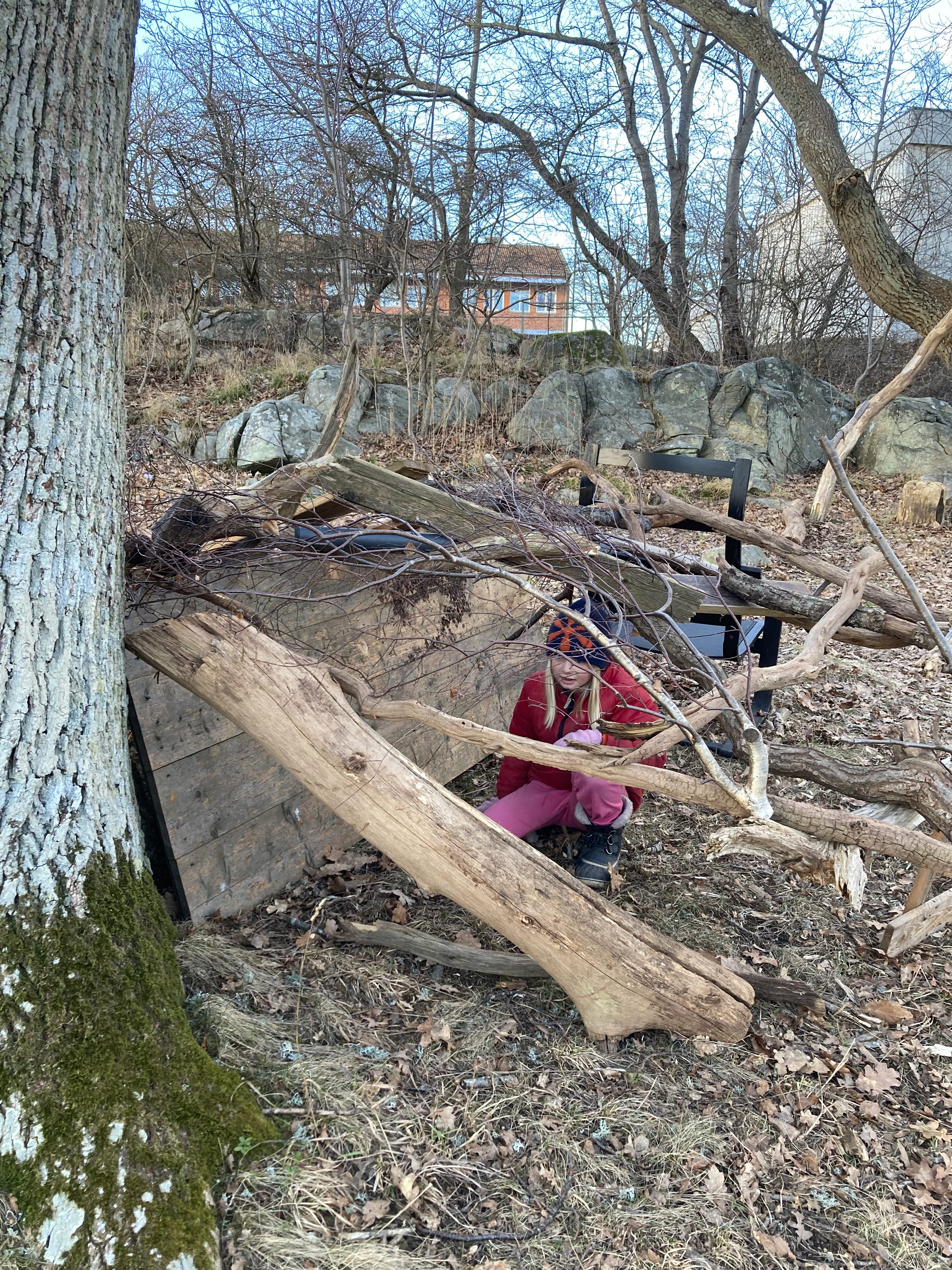 Flicka som leker i en koja som är skapad av upphittat naturligt material.