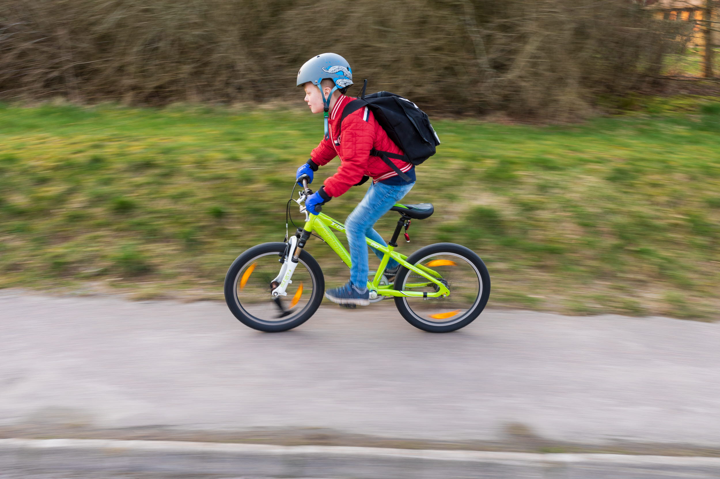 Pojke på grön cykel som cyklar på en trottoar.