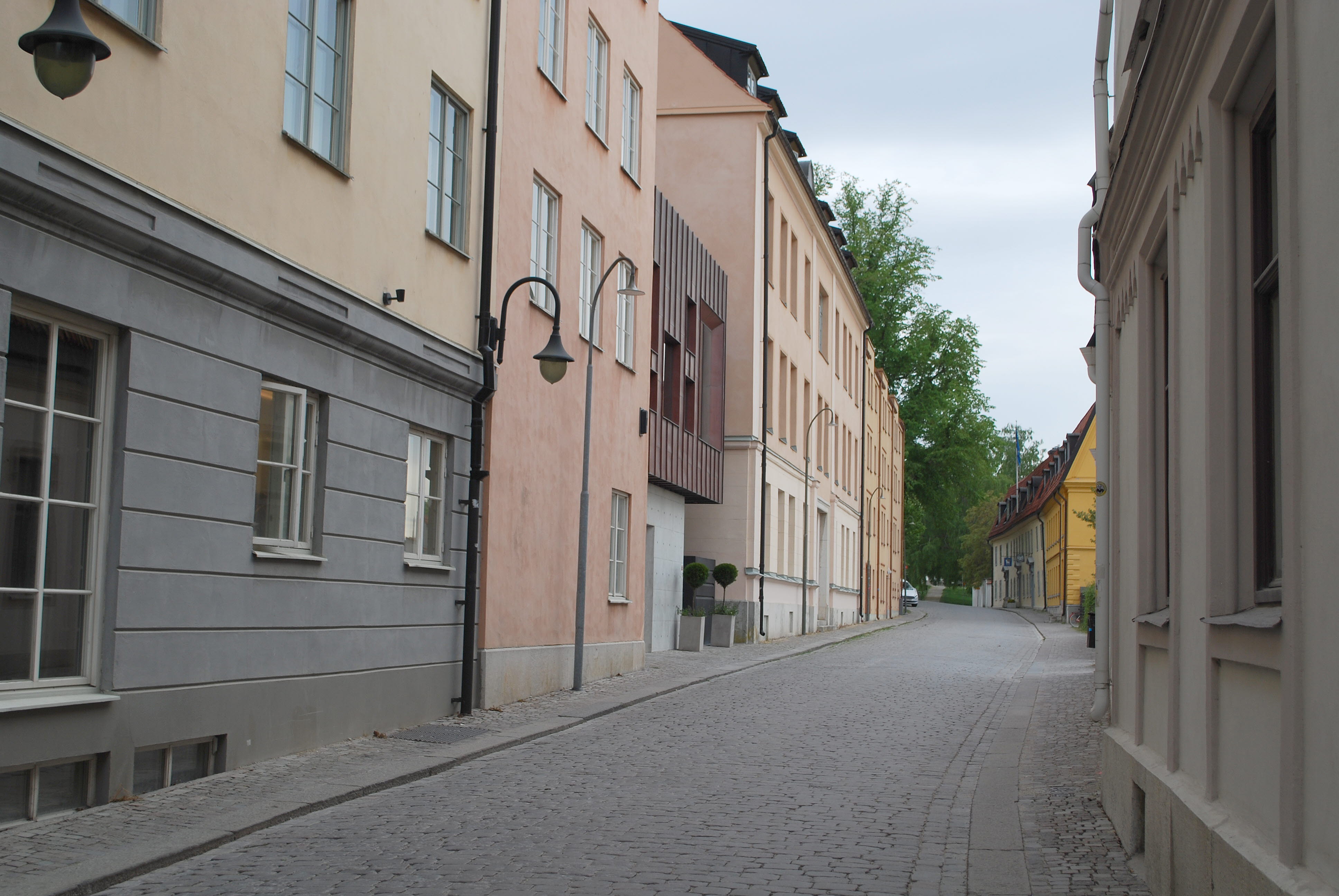 En gatstensbelagd gata med fastigheter på båda sidor. På vänstesidan syns en tillbyggnad i kopparplåt och betong.