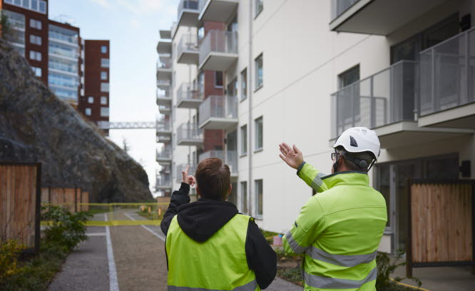 Två byggarbetare pekar och visar nybyggda flerbostadshus.