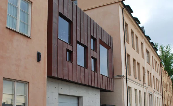 En gatstensbelagd gata med fastigheter på båda sidor. På vänstesidan syns en tillbyggnad i kopparplåt och betong.