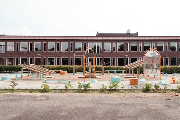 Lekplats framför en skolbyggnad, lekplatsen ligger väldigt nära skolbyggnaden.