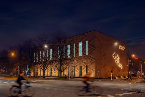 Upplyst fasad där belyssningen gör att teglets mönster framhävs.