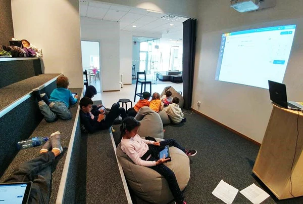 Barn som sitter på gradänger och sittpuffar i ett studierum.