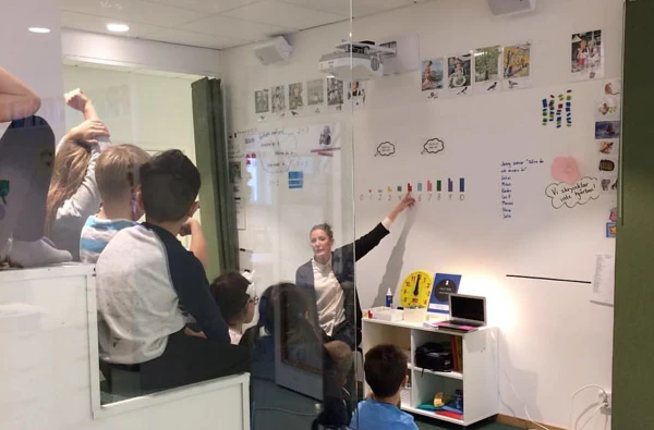 Elever som sitter på gradänger i olika nivåer och tittar på läraren som visar på tavlan.