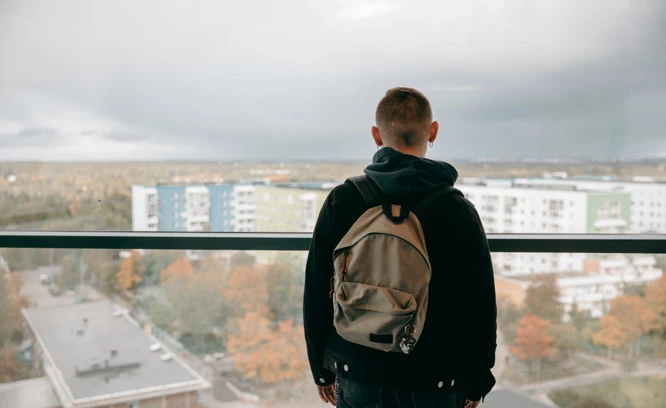 Ett barn står på en balkong och ser ut över ett bostadsområde. Foto: Scandinav