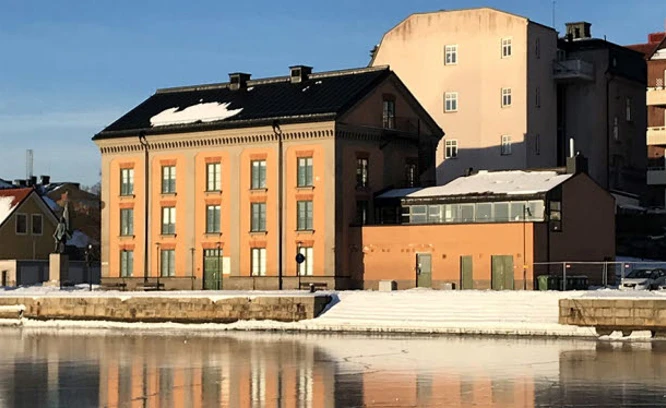 Äldre byggnader vid vatten med spegelblank is.