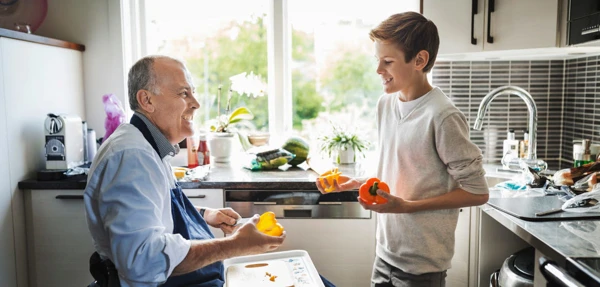 Pappa och son lagar mat i köket. Pappan använder rullstol. De är glada.